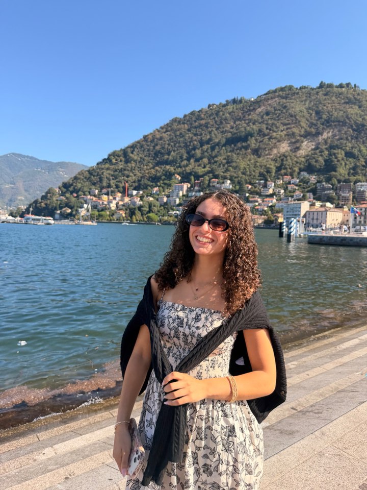 Norah Mehanna smiling beside a lakeside promenade with mountains in the background.